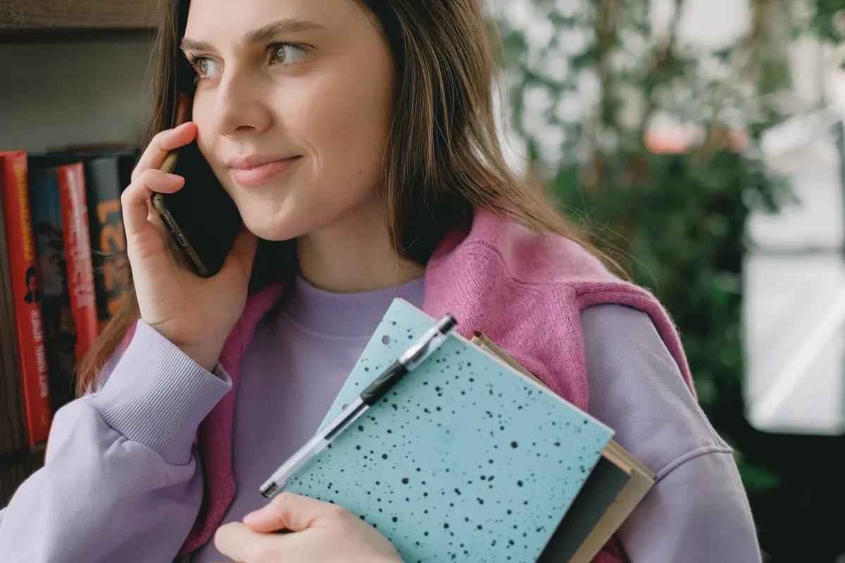 A woman speaks on the phone while holding a notebook.