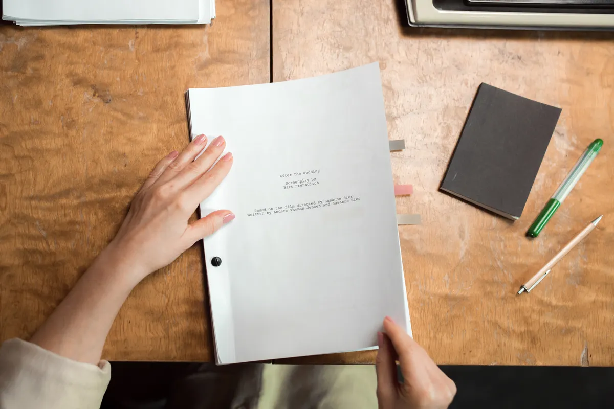 Hands organize documents, a notebook, and a pen on a desk.