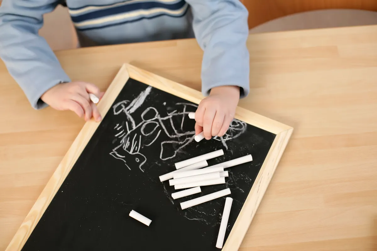 A child uses chalk on a blackboard to create a piece of work.