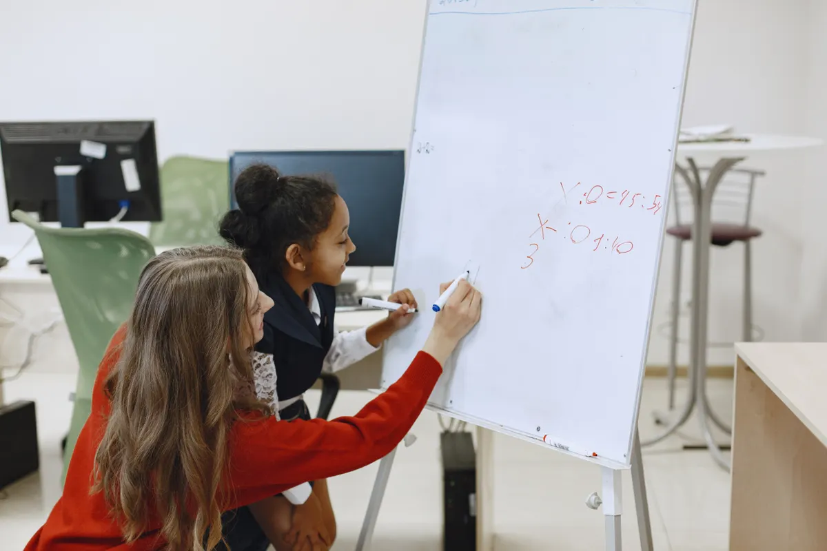 An adult helps a child work through math on a whiteboard.