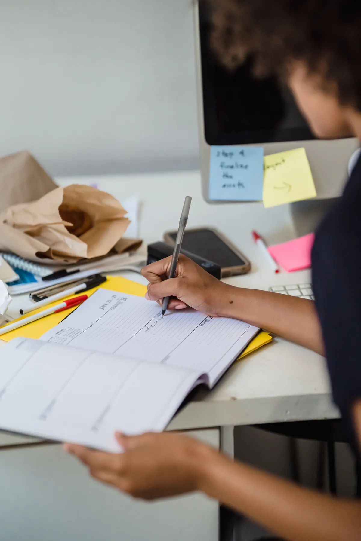 A woman records details in a planner at a desk.