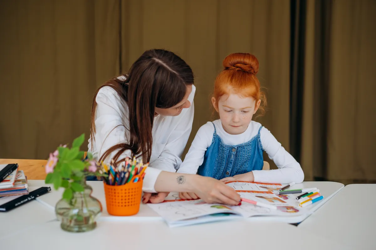 An adult supports a girl during a learning activity.