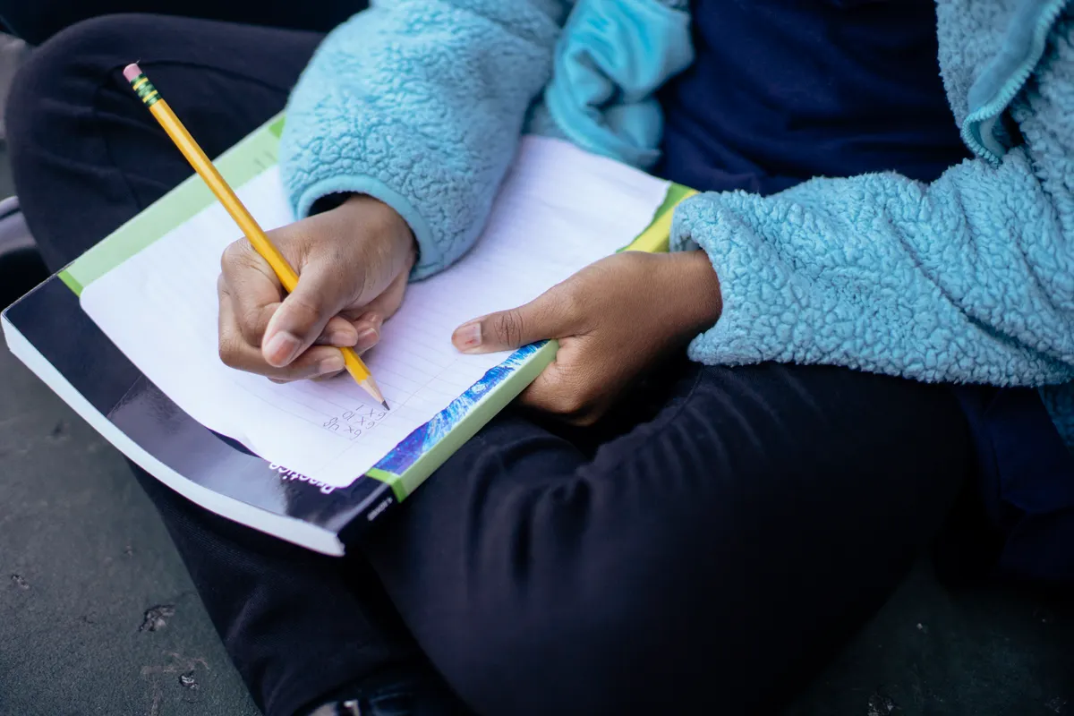 A child writes with a pencil on a sheet of paper.