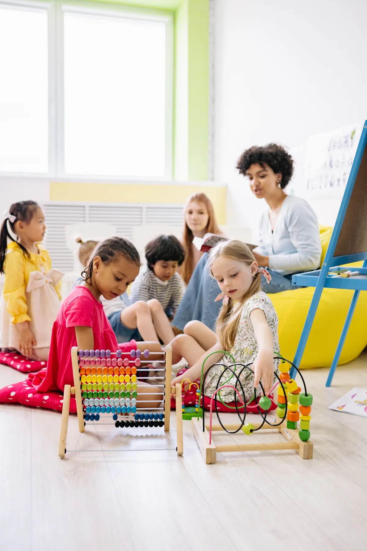 Children work with an abacus and other learning materials while a teacher sits nearby.