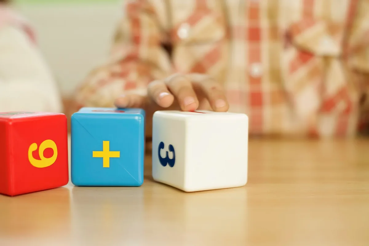 A child uses numbered blocks and an addition symbol for hands-on math.