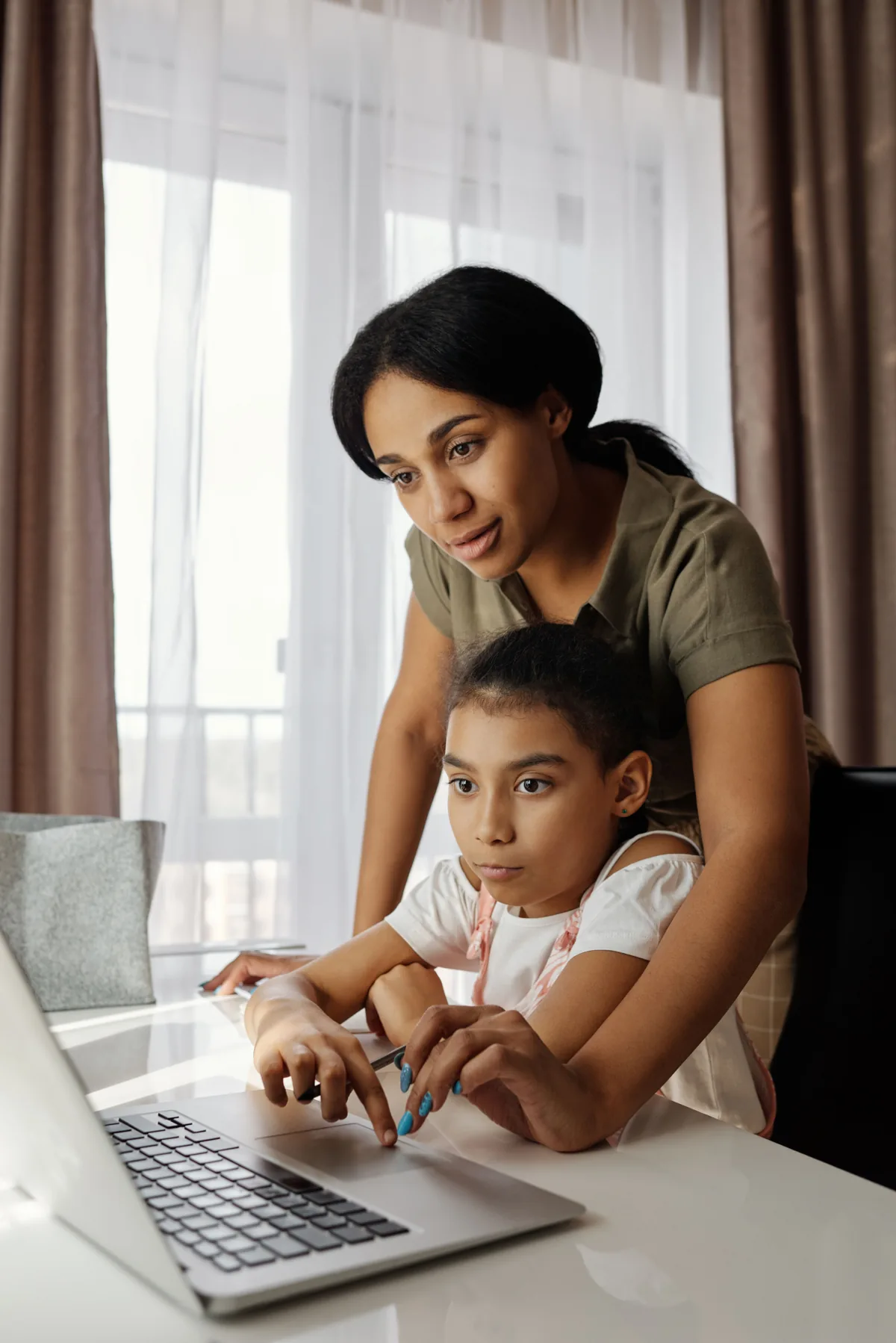 A mother helps her daughter follow a lesson on a laptop.
